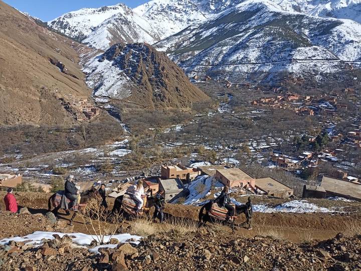 Caravan of mules carrying travellers through a snow-dusted Berber village in the Atlas foothills