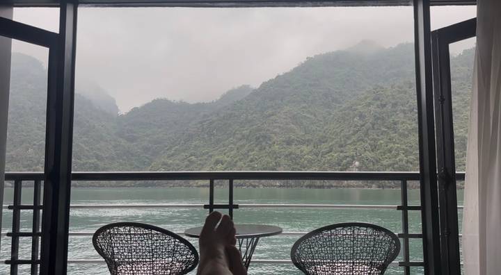 Relaxed view from cabin balcony toward misty limestone hills over tranquil bay.