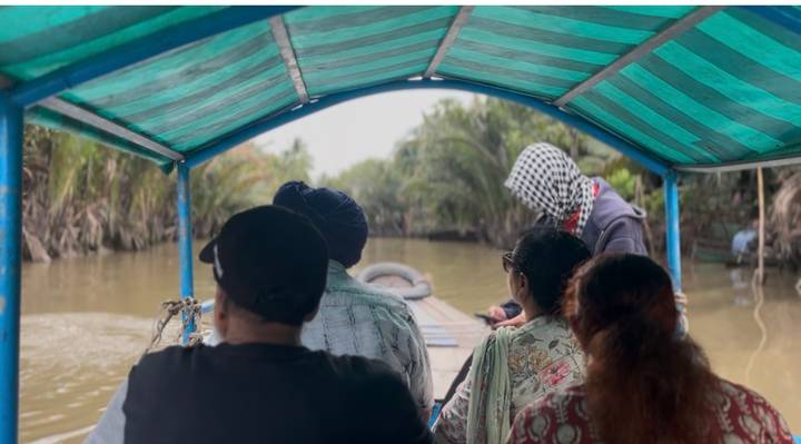 Small group rides under a striped canopy along a muddy jungle canal.