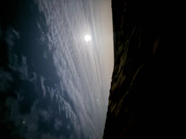 A dim night scene over desert dunes with the moon illuminating thin clouds.