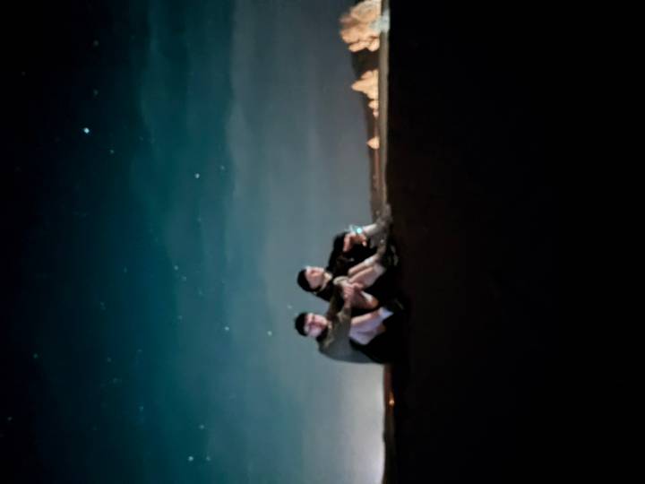 Two travelers sit on sand under a starry desert sky captured with significant blur.