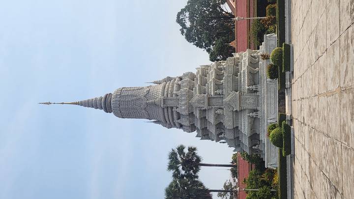 Ornate white stone stupa rises elegantly in a Cambodian temple complex framed by palms and manicured gardens.
