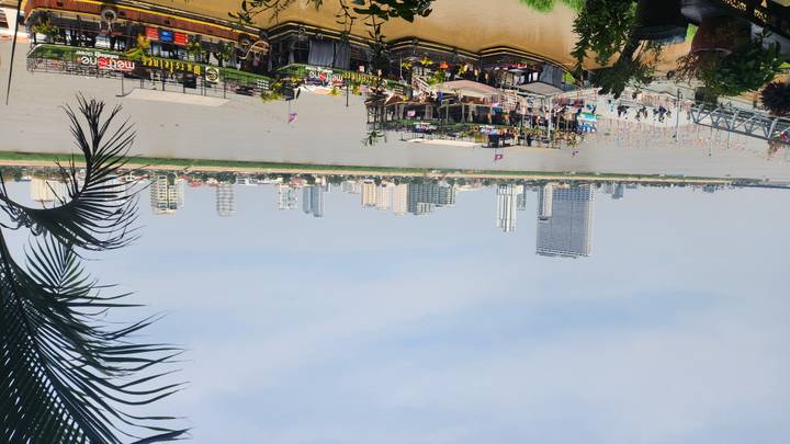 Panoramic view across a wide river toward Phnom Penh’s modern skyline with floating restaurants and boats along the waterfront.