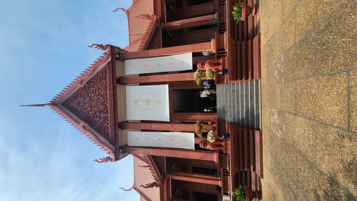Grand Khmer temple facade with steep red roof, twin lion statues and white decorative banners, seen from the foot of wide stone steps.
