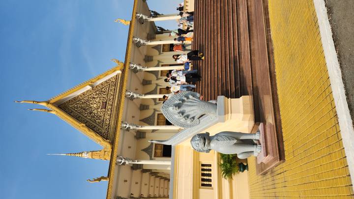 Elegant golden-trimmed temple with intricate gable and naga balustrades as visitors ascend the broad terracotta steps.