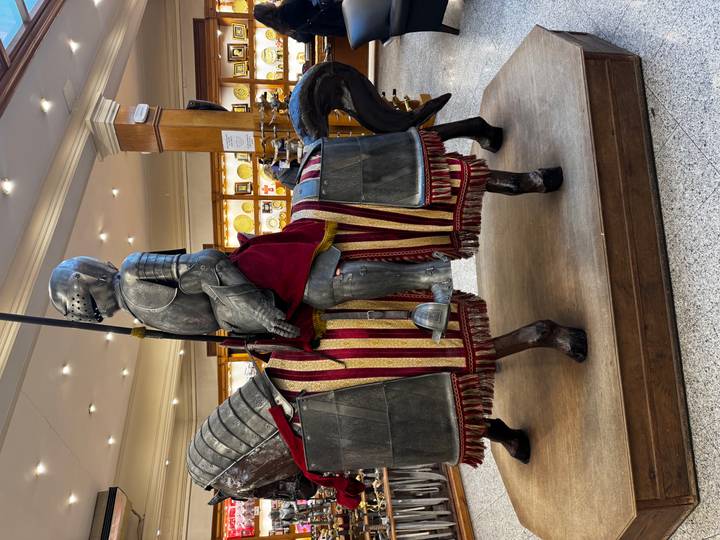 Full-size armored knight on a caparisoned horse displayed inside a brightly lit Spanish souvenir shop.