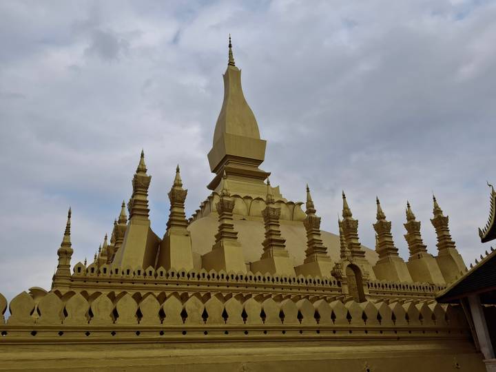 Golden spired stupa of Pha That Luang rising against a gray cloudy sky.