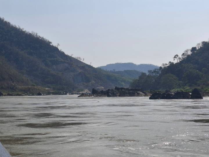 Wide river landscape with rocky hills under hazy sky.