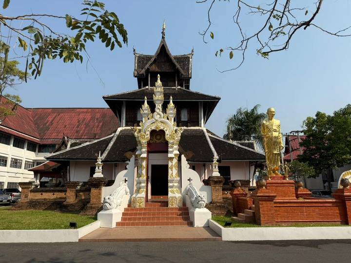 Traditional Buddhist temple with ornate gate and golden monk statue in courtyard.