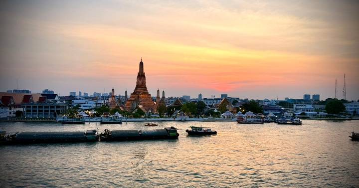 Fiery sunset over Wat Arun temple across the Chao Phraya River with boats below.