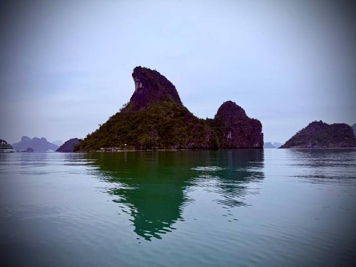 Distinctive limestone karst island reflecting on calm emerald water in Halong Bay.