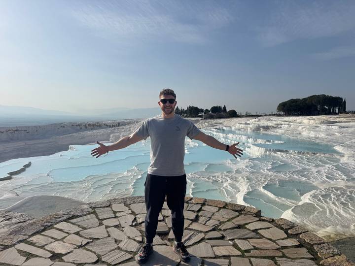 Traveler with arms outstretched in front of the white travertine pools of Pamukkale.