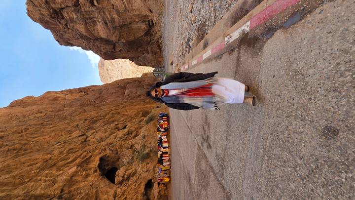 A lone visitor walks through the towering ochre cliffs of Todra Gorge, colourful scarves for sale lining the rock wall.