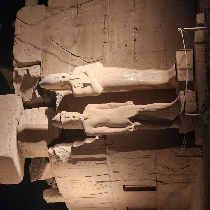 Two ancient statues lit by warm artificial light inside an Egyptian temple at night.