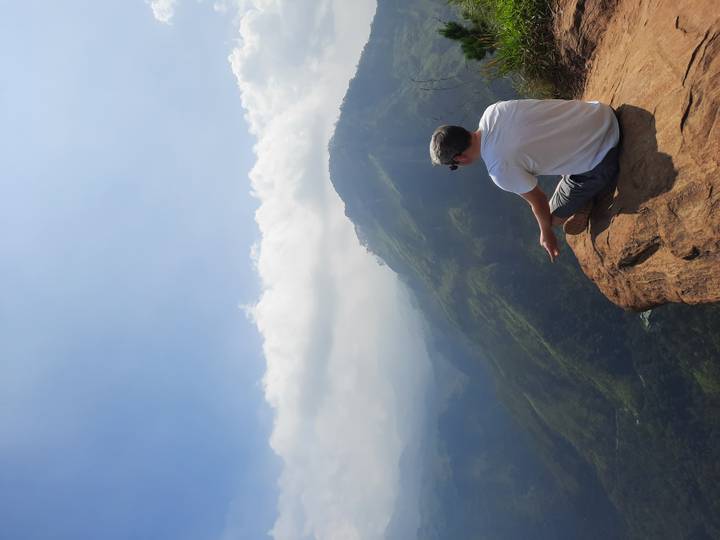 Man sits at the edge of a cliff meditating over misty green mountains near Ella