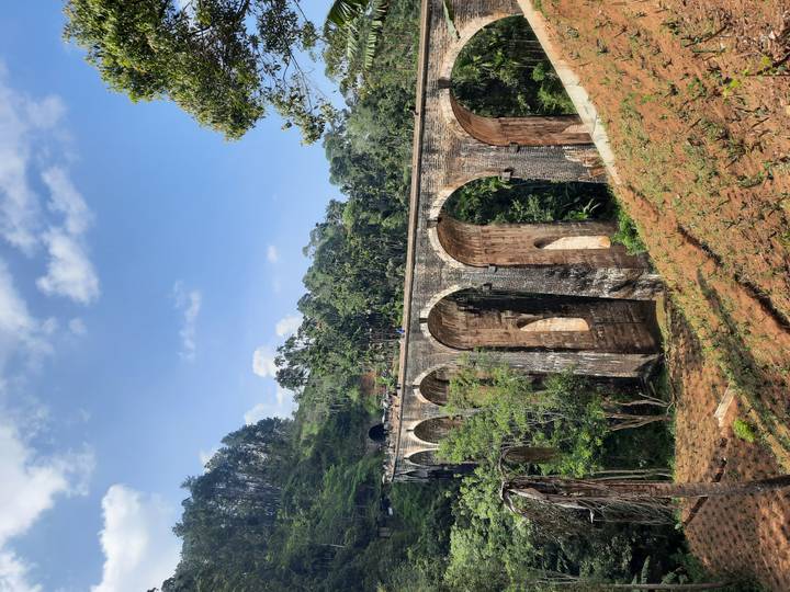 Historic Nine Arches Bridge stretches through lush jungle with tourists walking atop