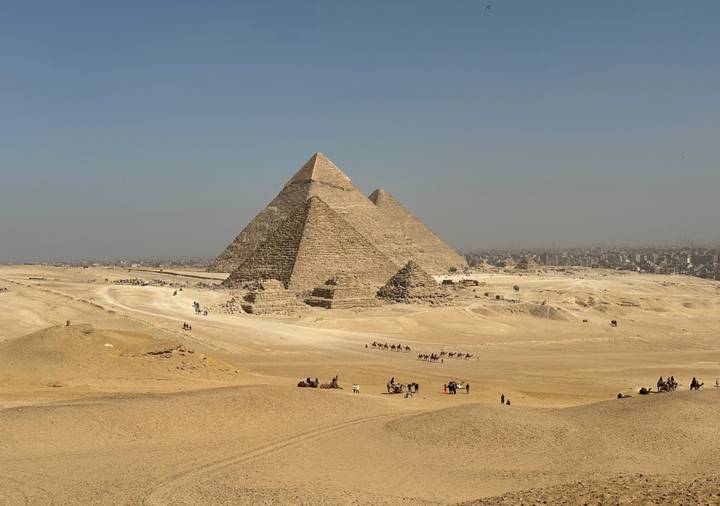 Iconic pyramids of Giza rising from the Egyptian desert with camel caravans below