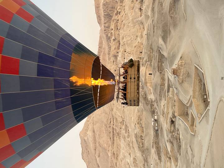 Hot-air balloon soars above desert ruins at dawn with a burst of flame lighting the colorful envelope.
