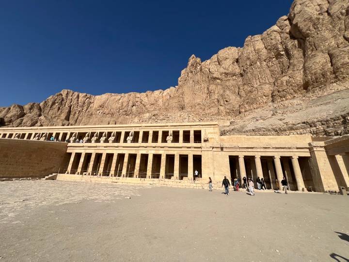Majestic Temple of Hatshepsut built into towering desert cliffs with small groups of visitors walking across the forecourt.