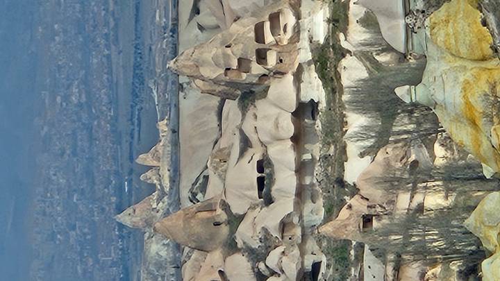 Unique volcanic rock formations and cave dwellings scatter the Cappadocian landscape with distant town visible below.