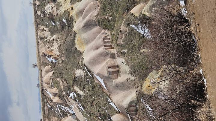 Snow-dusted rolling hills of soft volcanic tuff with abandoned cave houses in Cappadocia.