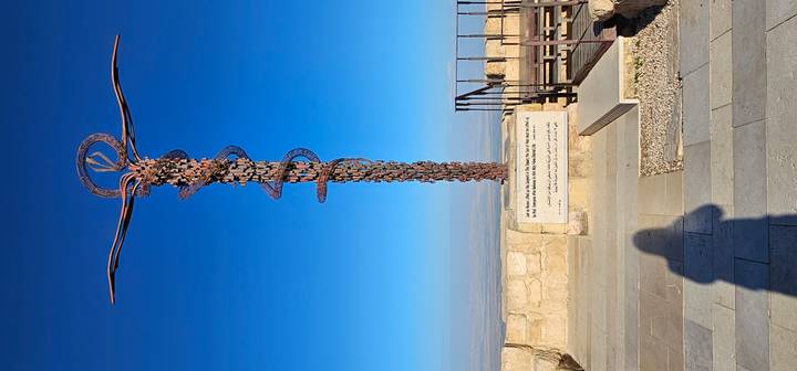 Serpentine bronze cross sculpture atop Mount Nebo against a deep blue sky with panoramic views below.