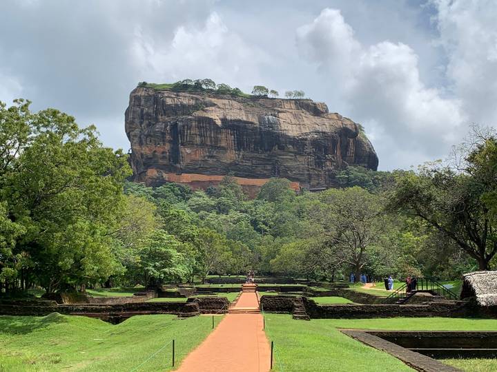 Iconic Sigiriya Rock Fortress rising above dense jungle with the ancient brick entrance path leading toward it.