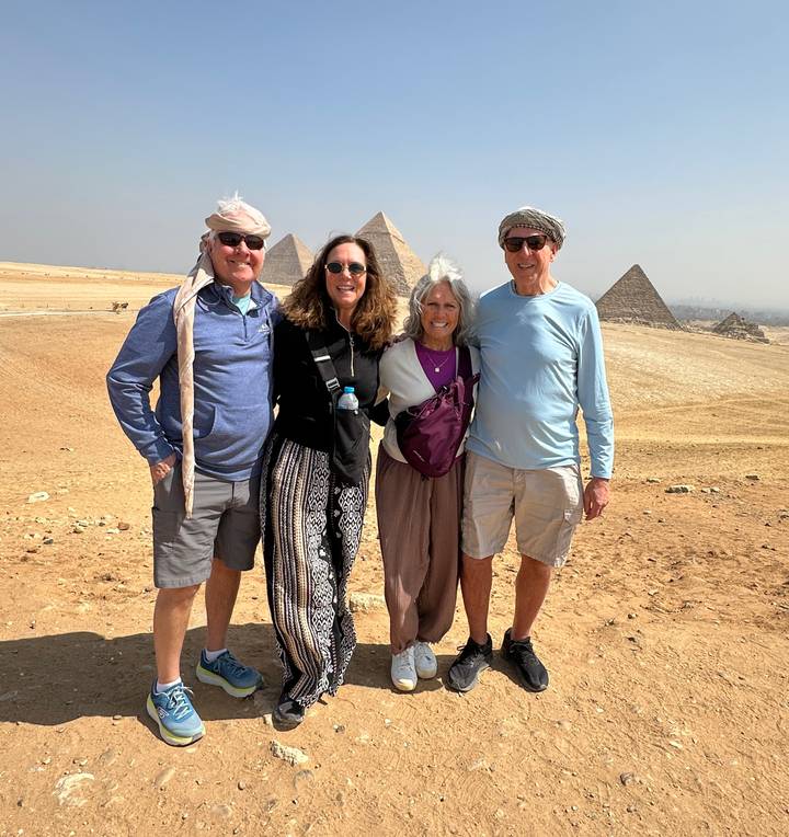 Four travelers smiling in front of the Pyramids of Giza on a bright desert day.