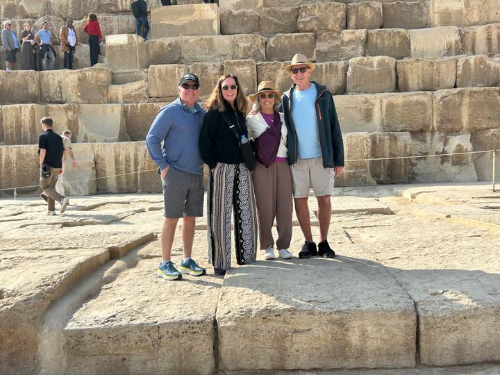 Tourists pose together on limestone blocks at the base of the Great Pyramid in Egypt.