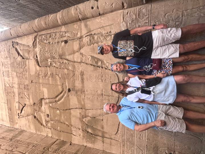 Group of four visitors standing in front of tall sandstone reliefs and hieroglyphics inside an ancient Egyptian temple.