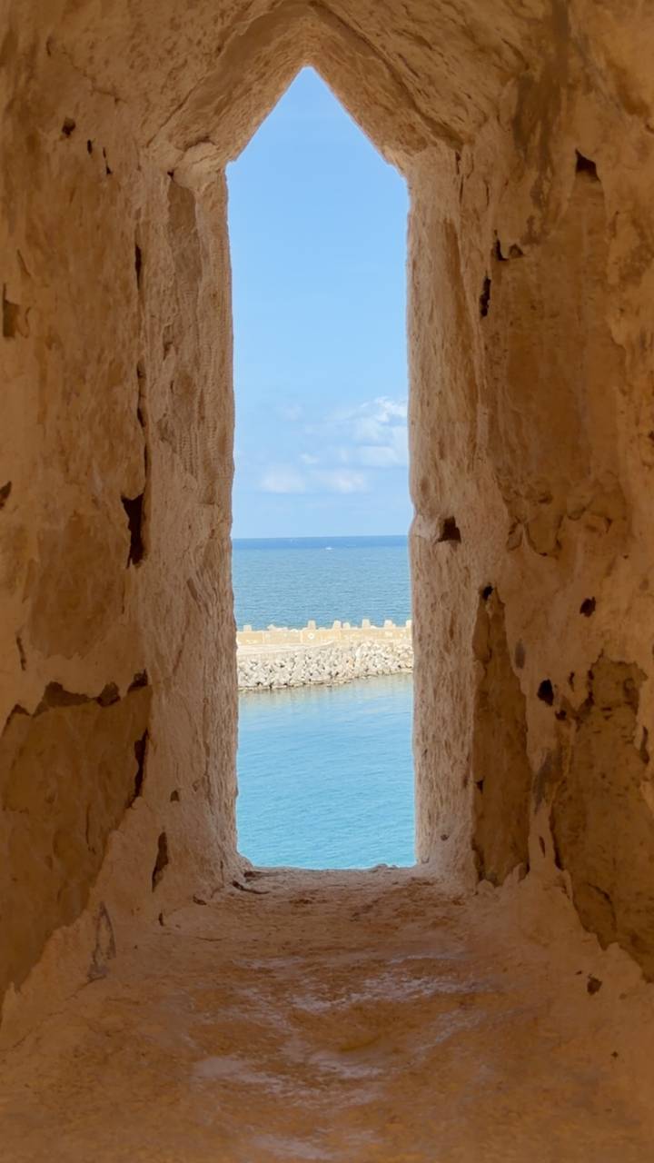 Blue sea framed through a narrow stone embrasure of an old seaside fort