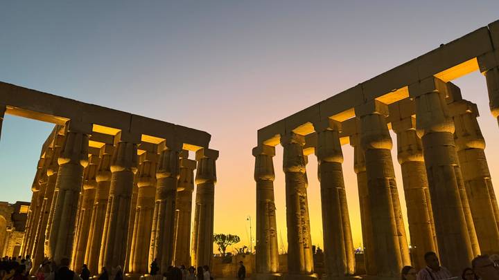 Illuminated columns of Luxor Temple glow against a vibrant sunset sky