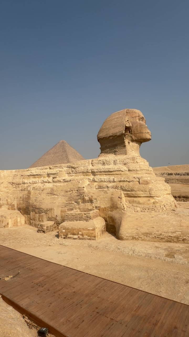 Side profile of the Great Sphinx with pyramid backdrop in the Giza desert