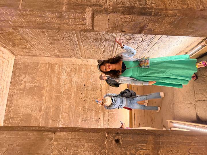 Visitor posing beside hieroglyphic-covered walls inside an ancient Egyptian temple as others take photos