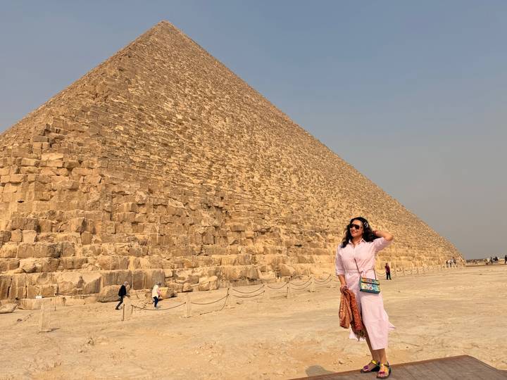 Woman standing beneath the towering limestone blocks of the Great Pyramid under a pale sky