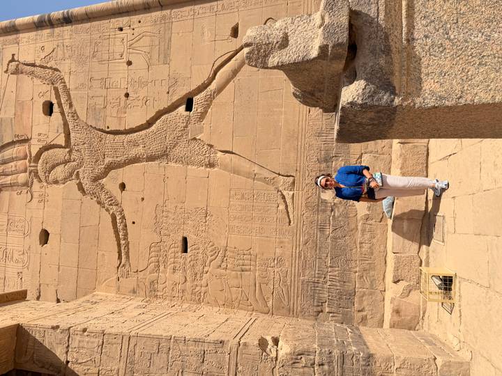 Visitor posing in front of colossal pharaonic relief carvings on sandstone temple walls