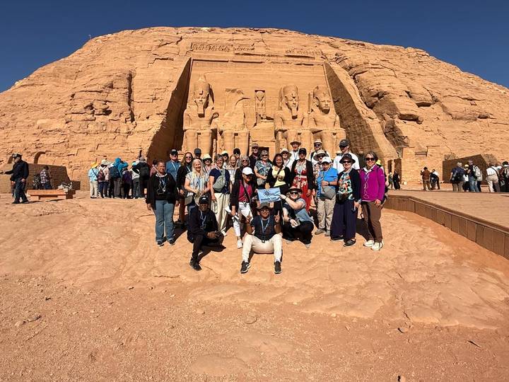 Tour group posing in front of the monumental Abu Simbel temple statues under a clear sky.