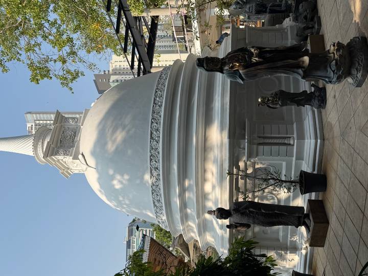 White stupa surrounded by modern city buildings and guardian statues in Colombo.
