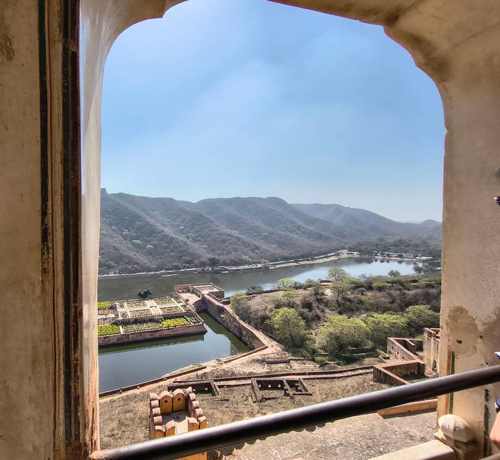 Scenic view through fort window overlooking a lake, ramparts and forested hills.