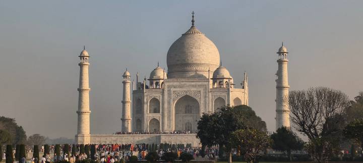 Classic symmetrical sunrise view of the Taj Mahal with soft light and crowds at its base.