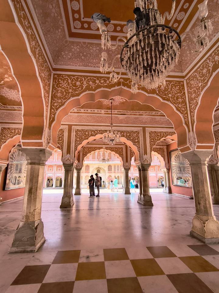 Ornate pink arches of Jaipur City Palace interior with chandeliers and visitors exploring.