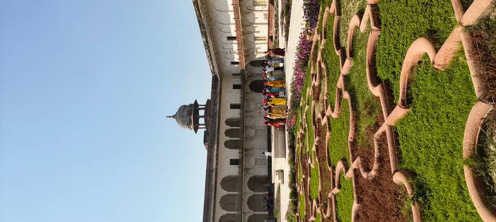 Courtyard garden of a historic Indian fort with a dome pavilion and a group of brightly dressed visitors
