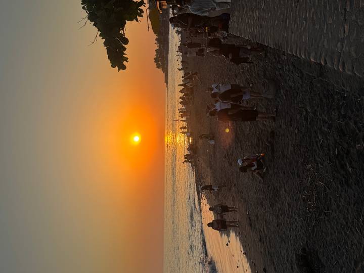 Crowd enjoying sunset on a dark sand beach with orange sun touching the horizon.