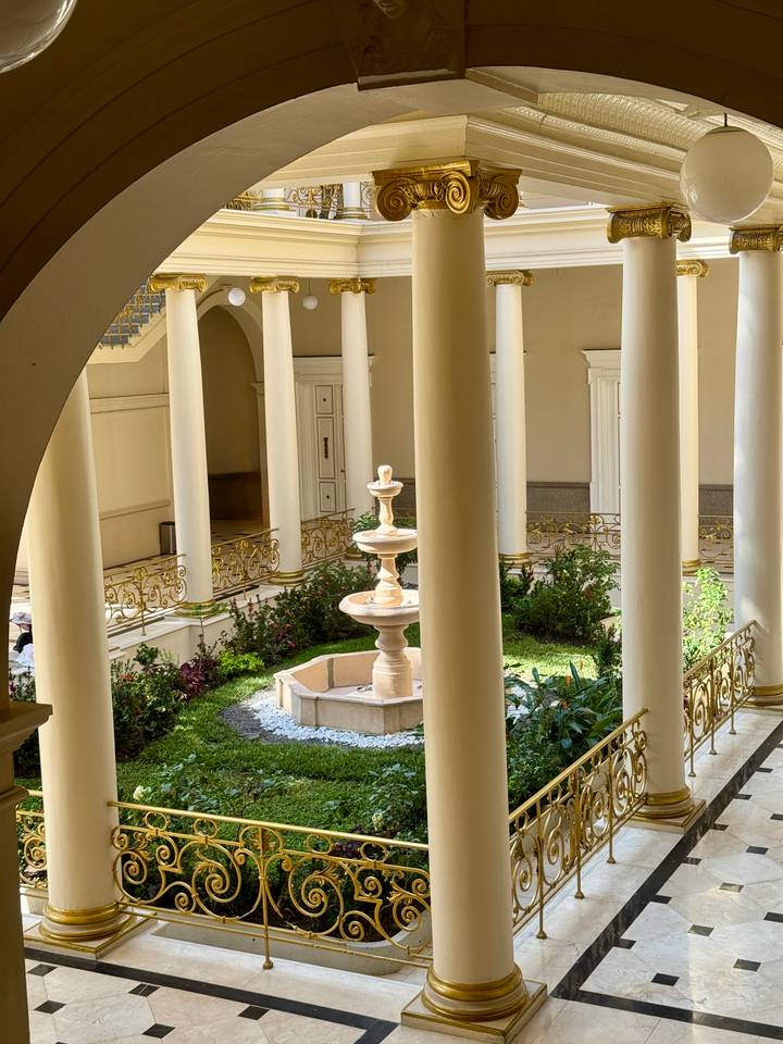 Elegant courtyard with central fountain surrounded by tall white columns and ornate railings.