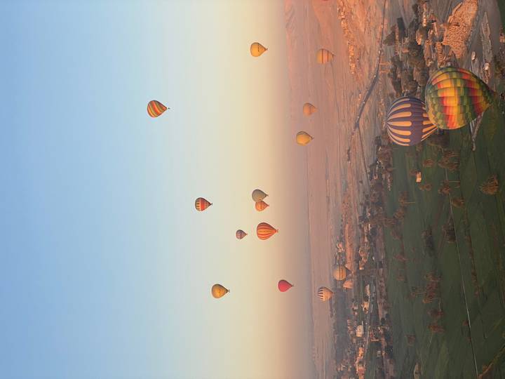 Dozens of colorful hot-air balloons drift above verdant fields at sunrise over Luxor.