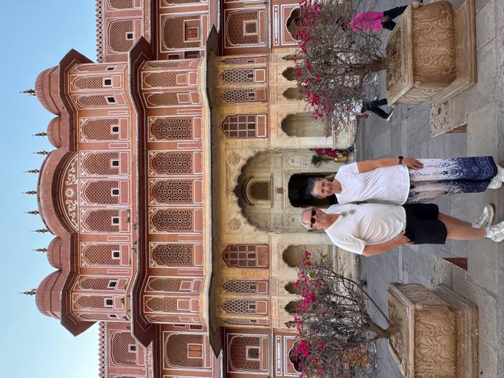 Couple stands in front of the ornate pink façade and latticed windows of Jaipur City Palace.