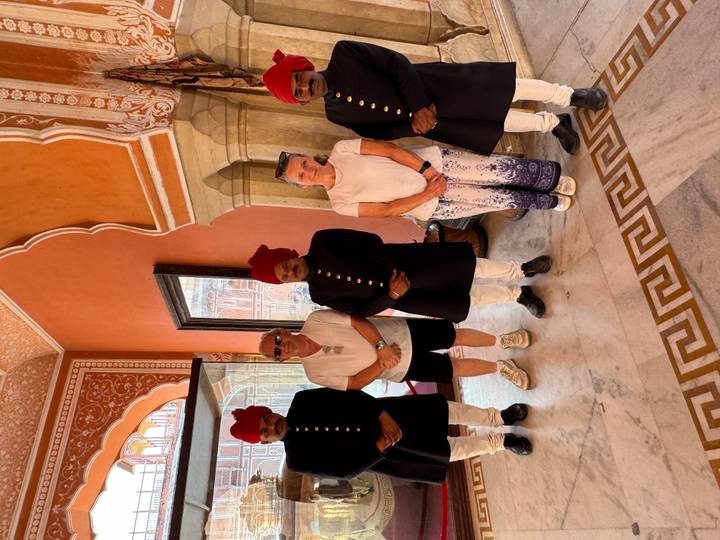 Visitors pose with traditionally dressed palace attendants in an ornately painted interior room.