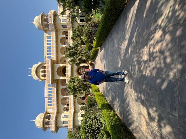 Man stands on a pathway leading to a grand palace-style hotel surrounded by manicured gardens.