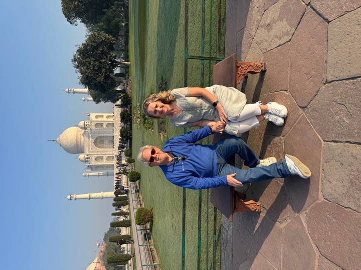 Couple sits on a bench with the iconic Taj Mahal perfectly framed in the morning light behind them.