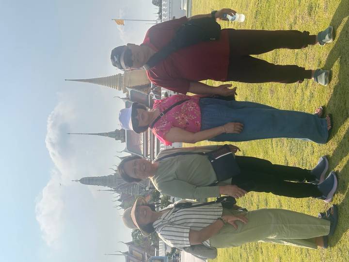 Friends posing on the lawn with the ornate spires of Bangkok’s Grand Palace in the background.